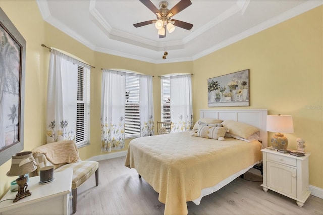 bedroom with light wood-style floors, baseboards, a tray ceiling, and ornamental molding