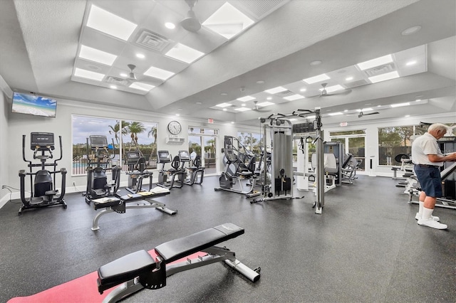 exercise room with a tray ceiling, visible vents, and baseboards