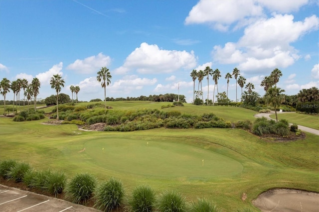 view of property's community featuring uncovered parking, view of golf course, and a lawn