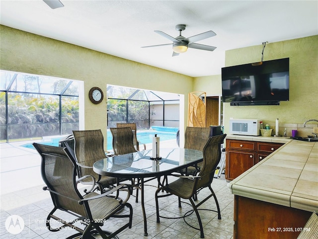 view of patio / terrace with a ceiling fan, a lanai, a swimming pool, a sink, and outdoor dining space