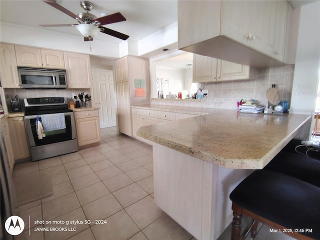 kitchen featuring light brown cabinets, stainless steel appliances, a peninsula, a kitchen breakfast bar, and backsplash