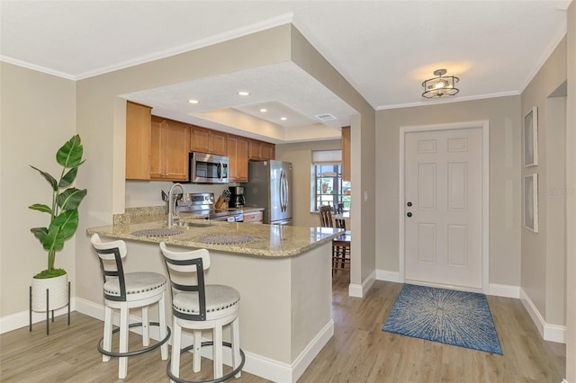 kitchen featuring appliances with stainless steel finishes, brown cabinets, light stone counters, a peninsula, and light wood-style floors