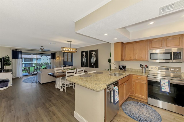 kitchen with visible vents, appliances with stainless steel finishes, open floor plan, a sink, and a peninsula