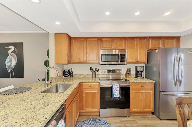 kitchen featuring light stone counters, light wood finished floors, appliances with stainless steel finishes, brown cabinetry, and a sink