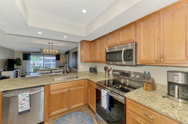 kitchen with stainless steel appliances, a peninsula, a sink, open floor plan, and a raised ceiling