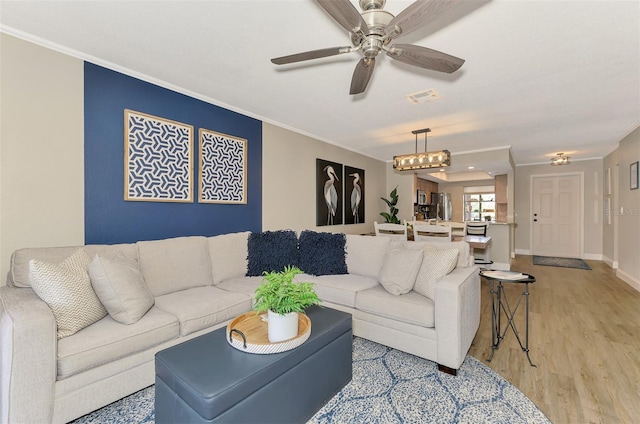 living area featuring light wood-style floors, baseboards, ornamental molding, and ceiling fan