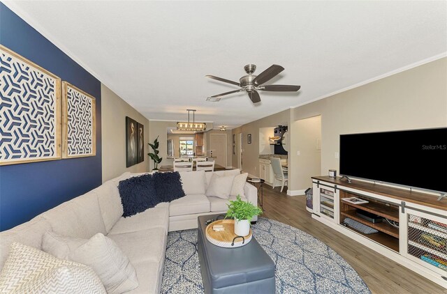 living area featuring ceiling fan with notable chandelier, ornamental molding, wood finished floors, and baseboards