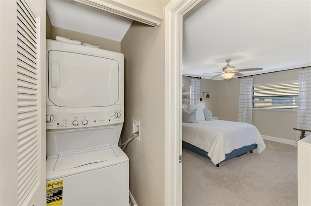 laundry area featuring light carpet, laundry area, a ceiling fan, baseboards, and stacked washer and clothes dryer