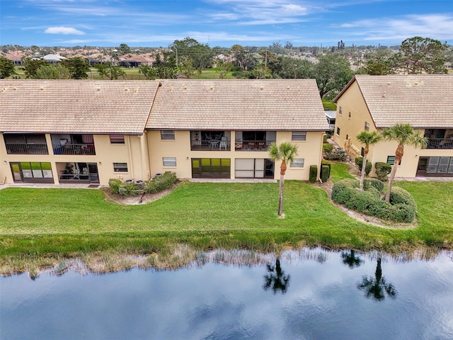 back of property featuring a water view, a yard, a tiled roof, and stucco siding