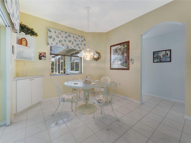 unfurnished dining area with arched walkways, light tile patterned floors, and baseboards