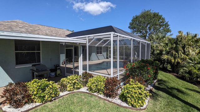 rear view of house with roof with shingles, stucco siding, a lawn, a patio area, and glass enclosure