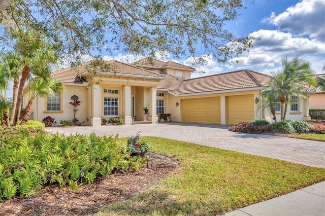 mediterranean / spanish-style home featuring a garage, a tiled roof, decorative driveway, and stucco siding