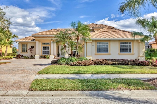 mediterranean / spanish-style home featuring a front lawn, decorative driveway, a tile roof, and stucco siding