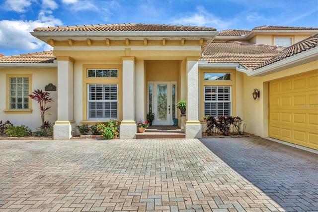 view of exterior entry with decorative driveway, a tiled roof, an attached garage, and stucco siding