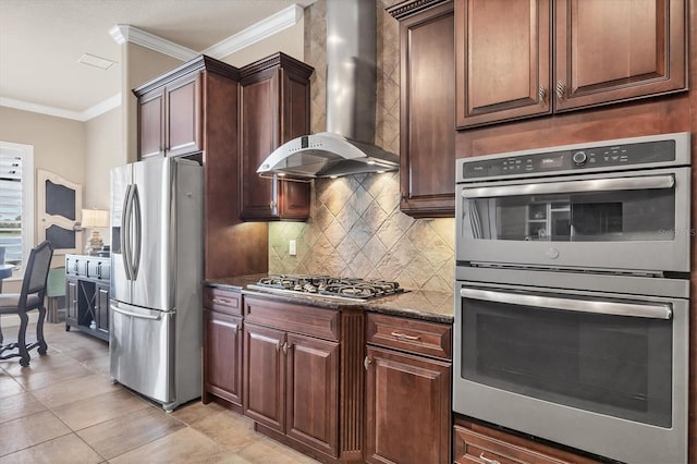 kitchen featuring dark stone counters, wall chimney exhaust hood, ornamental molding, stainless steel appliances, and backsplash