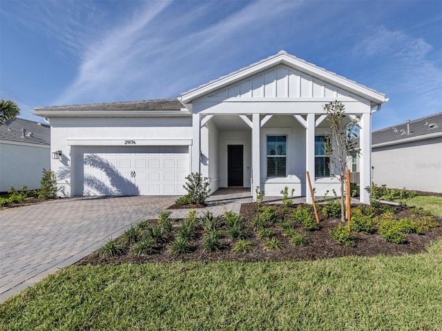 view of front of property with an attached garage, covered porch, decorative driveway, a front lawn, and board and batten siding