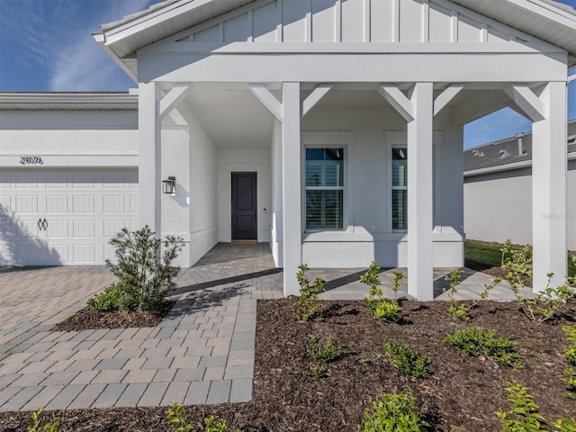 property entrance featuring decorative driveway, board and batten siding, an attached garage, and stucco siding