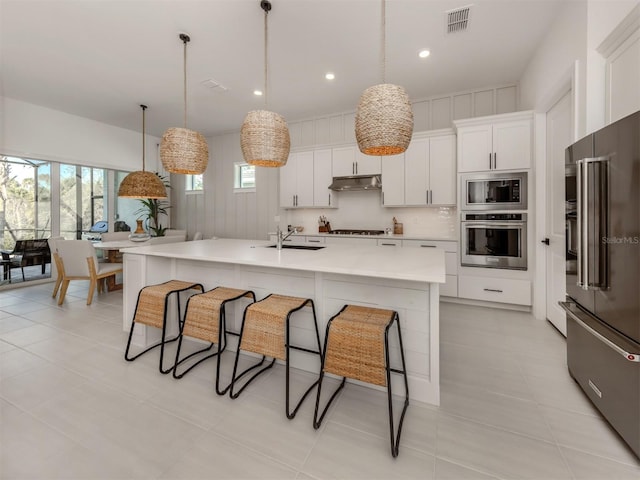 kitchen with stainless steel appliances, visible vents, white cabinetry, light countertops, and an island with sink