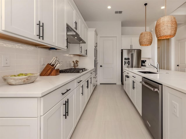 kitchen featuring under cabinet range hood, stainless steel appliances, a sink, visible vents, and decorative light fixtures