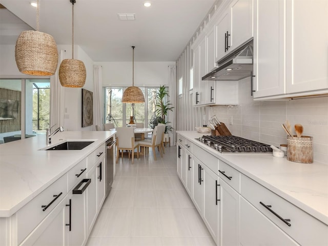 kitchen with under cabinet range hood, a sink, white cabinets, appliances with stainless steel finishes, and decorative light fixtures