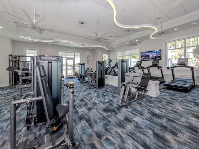 workout area featuring a tray ceiling, a healthy amount of sunlight, visible vents, and ceiling fan