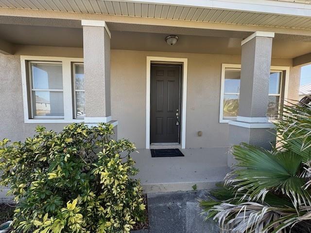 doorway to property with a porch and stucco siding