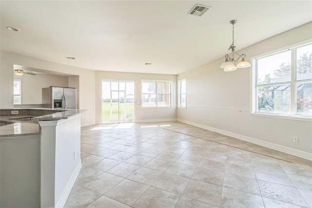 kitchen featuring stainless steel refrigerator with ice dispenser, visible vents, hanging light fixtures, stone countertops, and baseboards