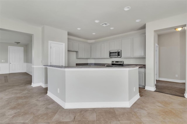 kitchen featuring baseboards, visible vents, a center island, gray cabinets, and stainless steel appliances