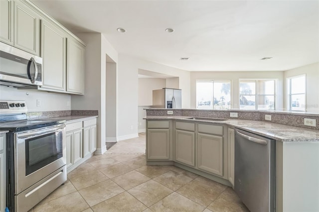 kitchen with appliances with stainless steel finishes, light tile patterned flooring, light stone countertops, and gray cabinetry