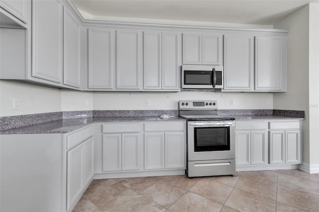 kitchen with appliances with stainless steel finishes, dark stone counters, white cabinets, and light tile patterned flooring