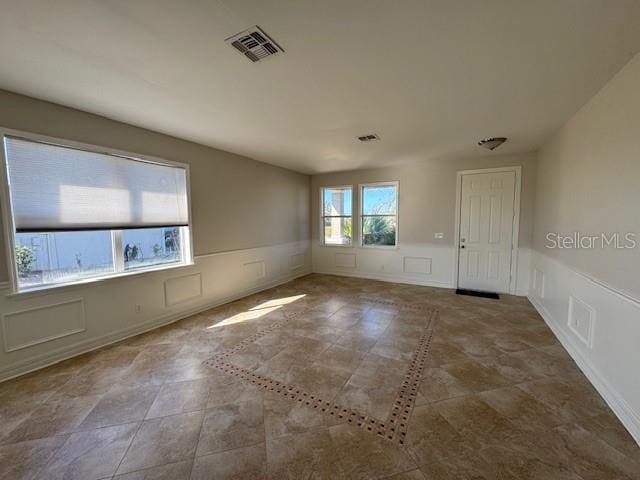 empty room featuring a wainscoted wall, visible vents, and a decorative wall