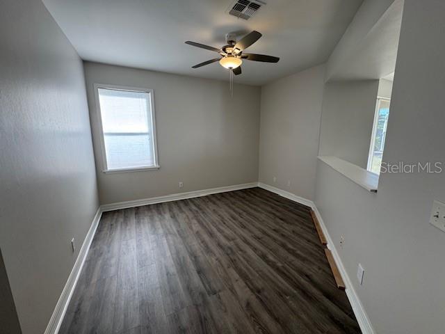 spare room with dark wood-style floors, ceiling fan, visible vents, and baseboards