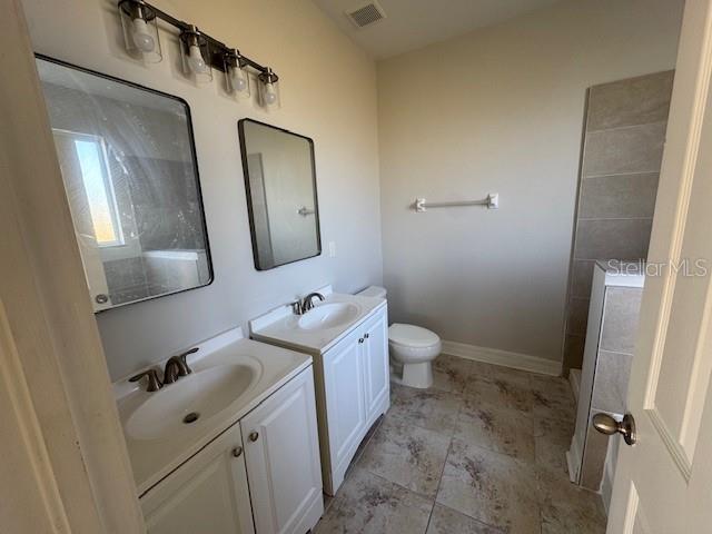 bathroom with two vanities, visible vents, toilet, a sink, and baseboards