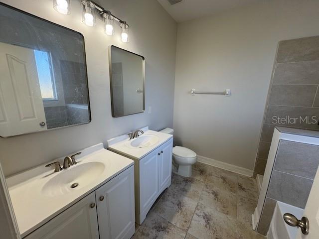 full bath featuring toilet, two vanities, a sink, and baseboards