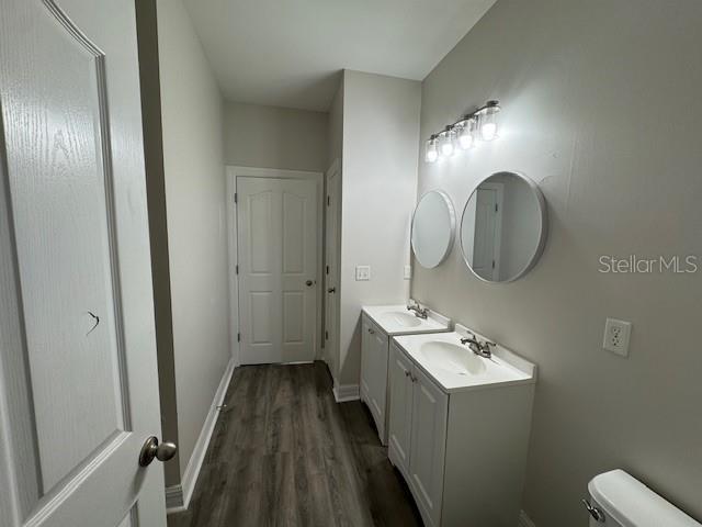 bathroom featuring two vanities, a sink, baseboards, and wood finished floors