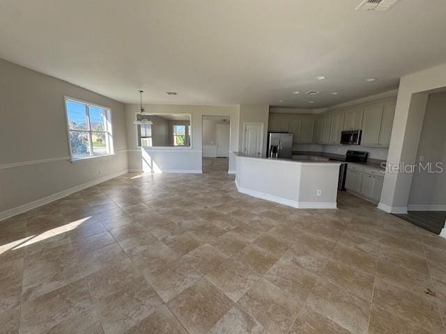 kitchen featuring pendant lighting, stainless steel appliances, open floor plan, an island with sink, and baseboards