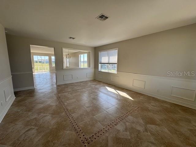 unfurnished room with a wealth of natural light, visible vents, and a decorative wall