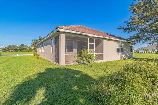 rear view of property featuring a yard, a tile roof, a sunroom, and stucco siding