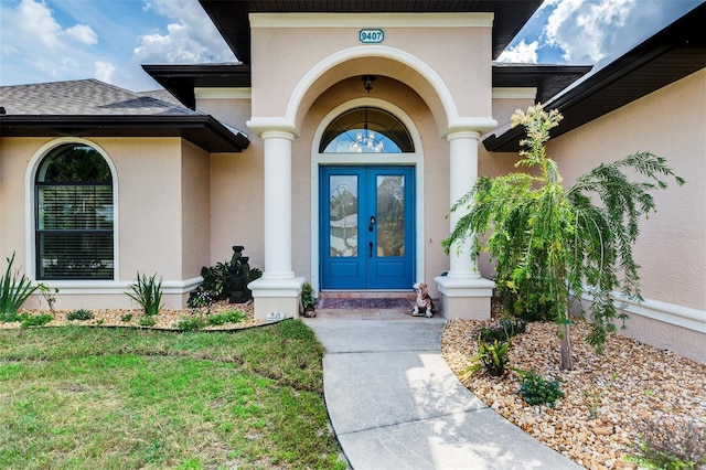 property entrance with french doors, a lawn, a shingled roof, and stucco siding