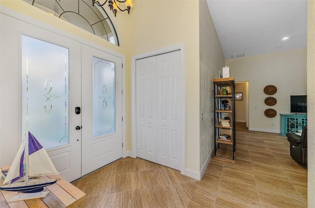 foyer featuring baseboards, a high ceiling, and visible vents