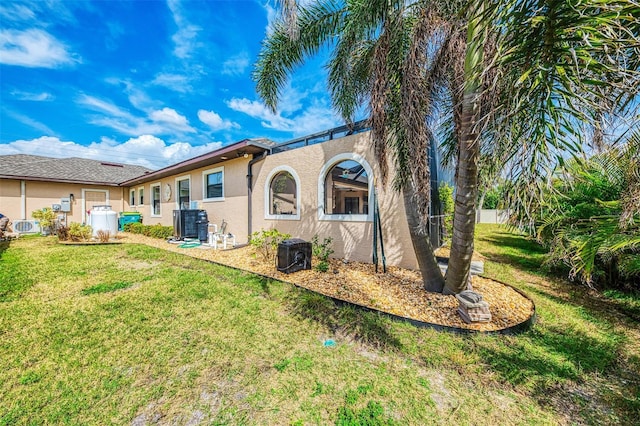 back of property with a yard, central AC, and stucco siding