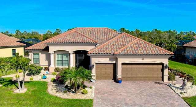 mediterranean / spanish-style house featuring an attached garage, stucco siding, decorative driveway, and a tiled roof