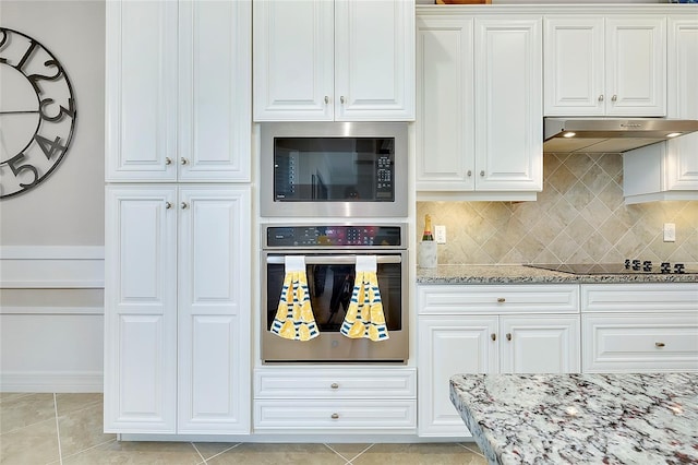 kitchen featuring stainless steel appliances, under cabinet range hood, light stone counters, and light tile patterned floors