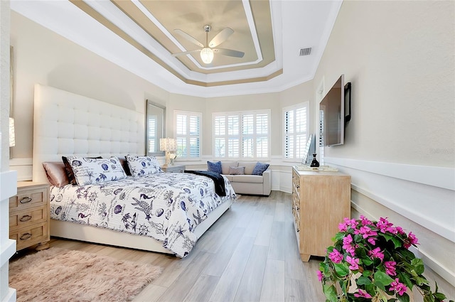 bedroom with light wood-style flooring, visible vents, a ceiling fan, ornamental molding, and a raised ceiling