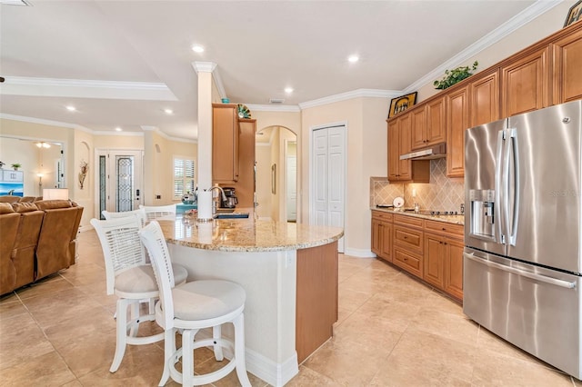 kitchen with stainless steel fridge, arched walkways, a breakfast bar, under cabinet range hood, and a sink