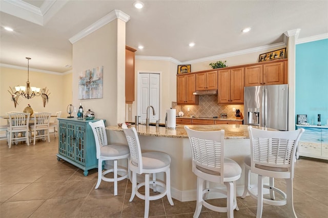 kitchen featuring crown molding, light stone counters, stainless steel fridge, and decorative backsplash