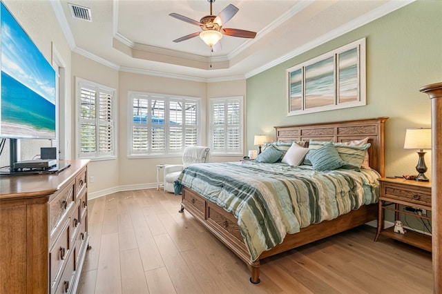 bedroom featuring a tray ceiling, multiple windows, and light wood finished floors