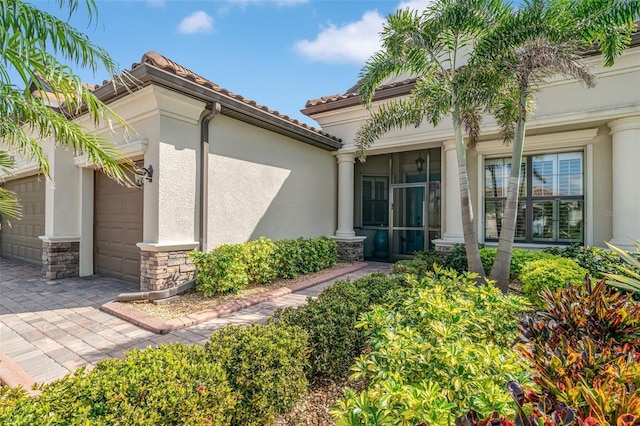 property entrance with an attached garage, stone siding, a tile roof, and stucco siding