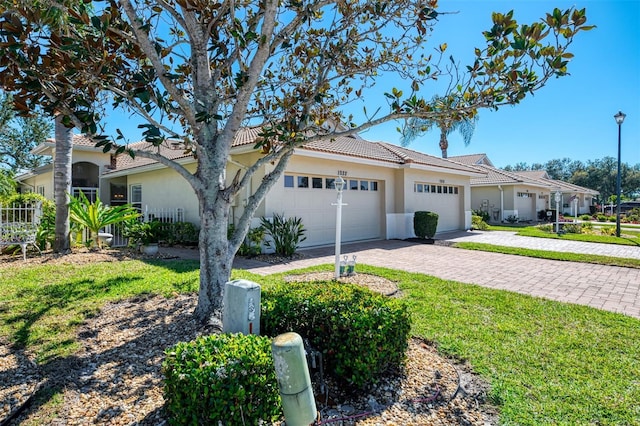 view of front of home featuring a front lawn, a tiled roof, stucco siding, decorative driveway, and a garage