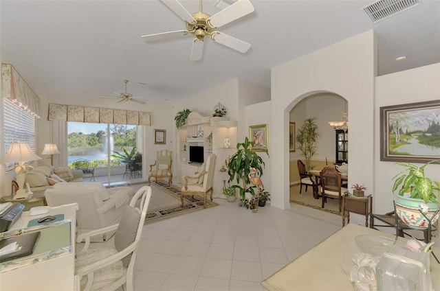 living room featuring visible vents, a ceiling fan, arched walkways, light tile patterned floors, and vaulted ceiling